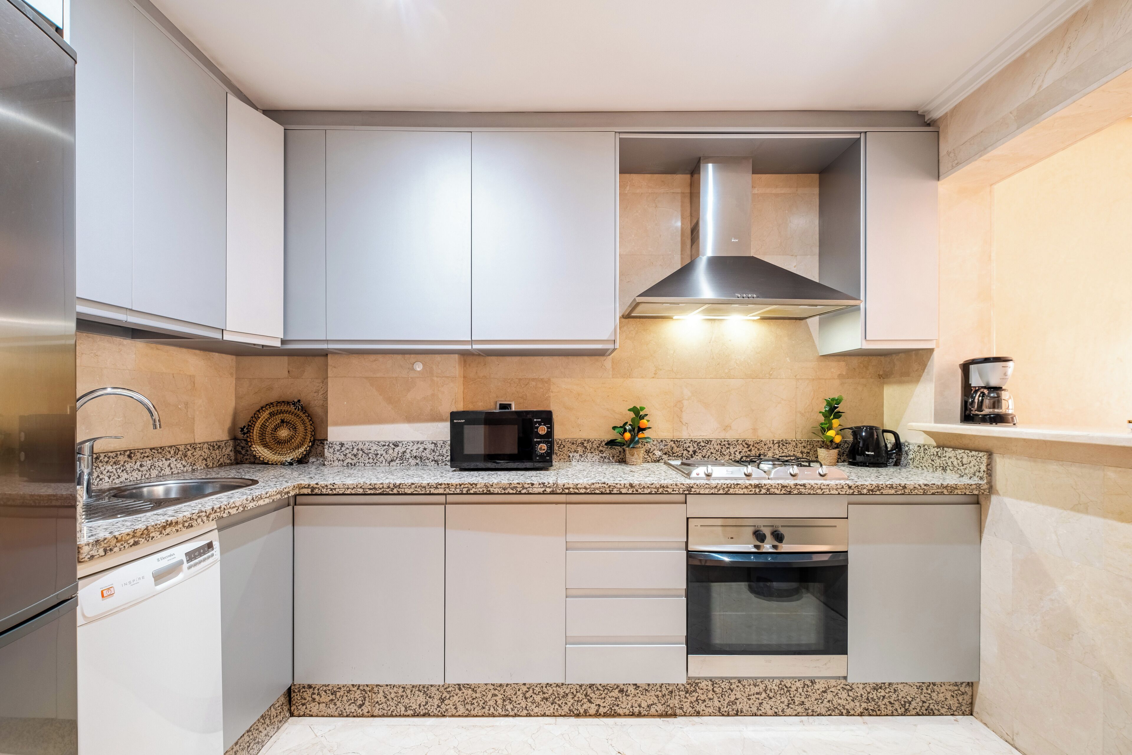 A modern kitchen with white cabinets, a stainless steel range hood, a microwave, a sink, and a built-in oven.