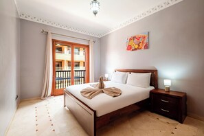 A hotel room with a double bed, a bedside table with a lamp, a window with curtains, a balcony, and a decorative wall piece. - Hyper Centre Plaza Balcony & Parking (Marrakech)