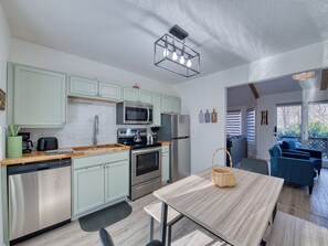 A modern kitchen with stainless steel appliances, a dining area with a light wood table, and a view to a balcony. - Easy Access Cottage - Pet-Friendly -Maggie Valley. (Maggie Valley)