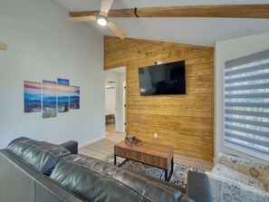 Ein Wohnzimmer mit einer Ledersofa, einem Holztisch und einem flachbildschirmfernseher an einer Holzwand.