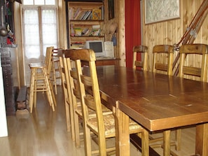 Uma sala de jantar com uma mesa e cadeiras de madeira, uma estante e um computador.