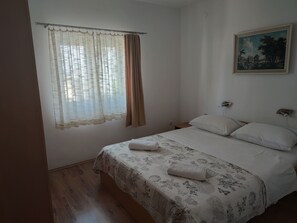 A bedroom with a bed, a window with curtains, a painting on the wall, and a wooden floor. - Your Perfect Summer Getaway in Croatia (Krk)