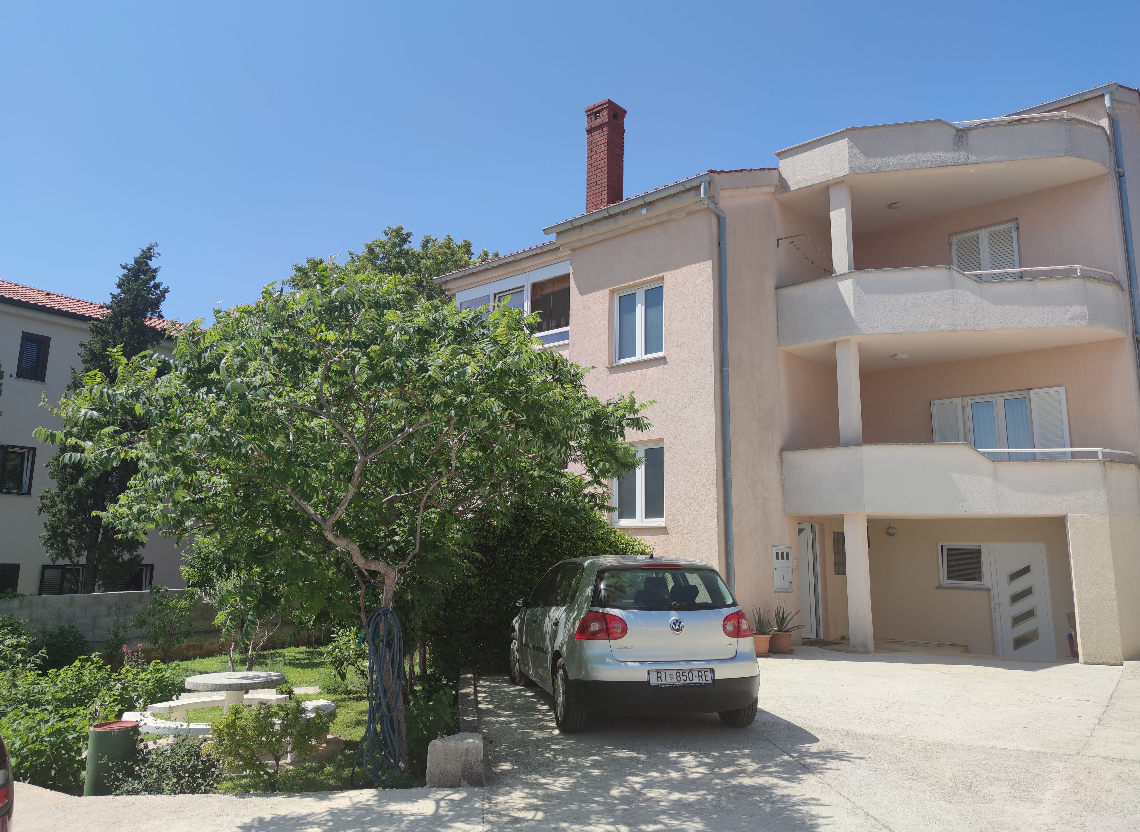 A residential building with a car parked in front, a tree, and a clear sky.