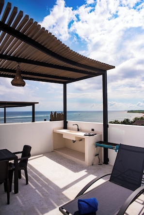 Un balcón con vista al mar, un lavabo y una silla.