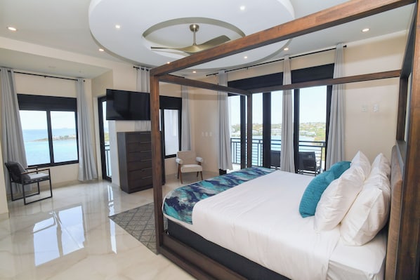 A modern bedroom with a large bed, a TV, and a balcony with a view.