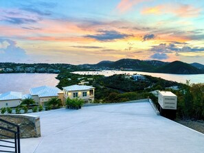 A coastal property with a view of the sea and hills, featuring modern buildings and a paved area.