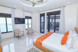 Una camera d'albergo con un letto, due poltrone, una TV e ampie finestre vista mare.