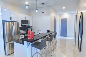 A modern kitchen with stainless steel appliances, a black countertop, and bar stools.