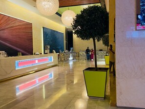 En hotellobby med en receptionsdisk, en stor plantering med ett träd och ett marmorgolv.