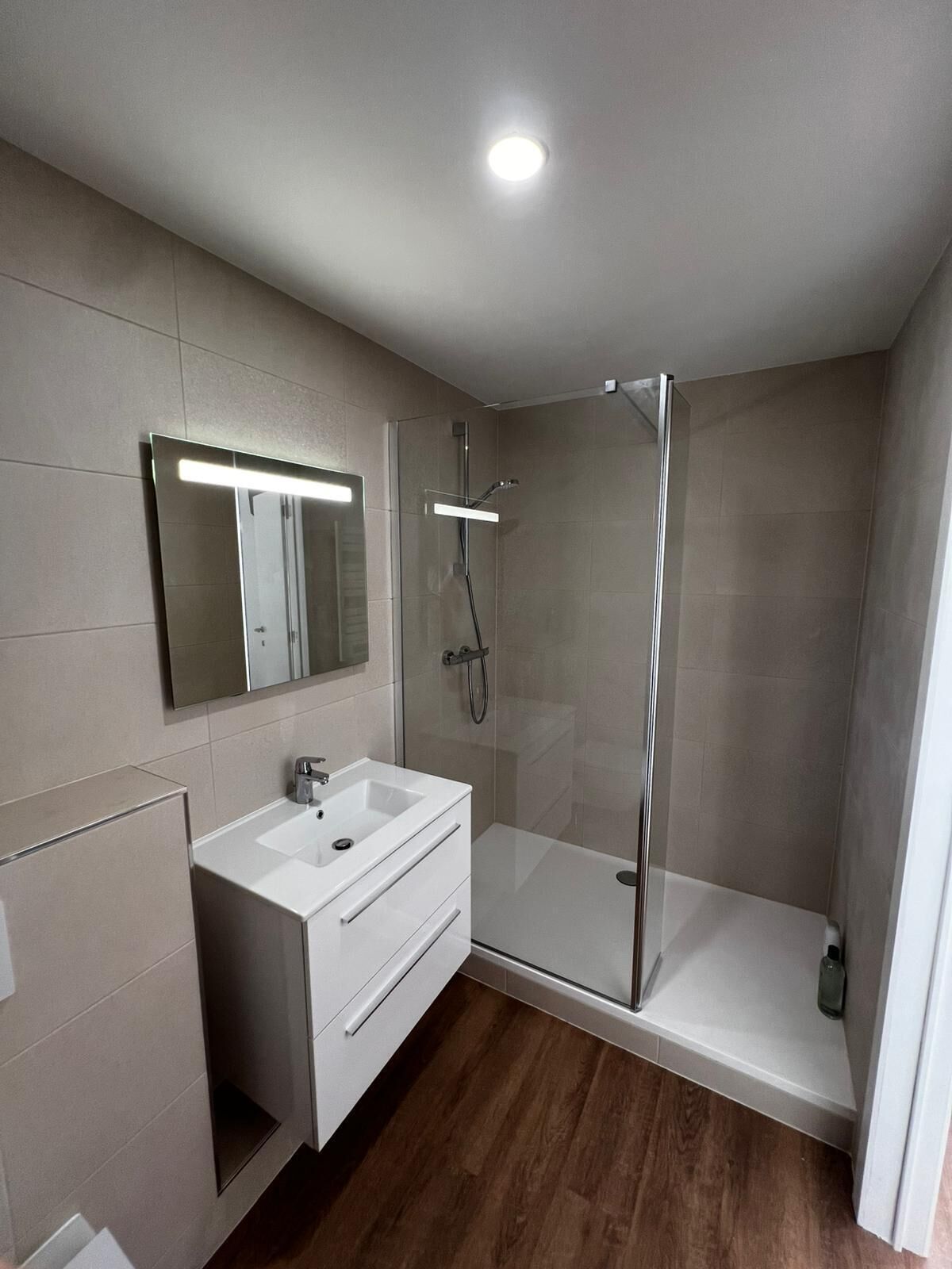 Une salle de bain moderne avec une douche à parois de verre, un meuble-lavabo blanc avec un miroir et un éclairage encastré au plafond.