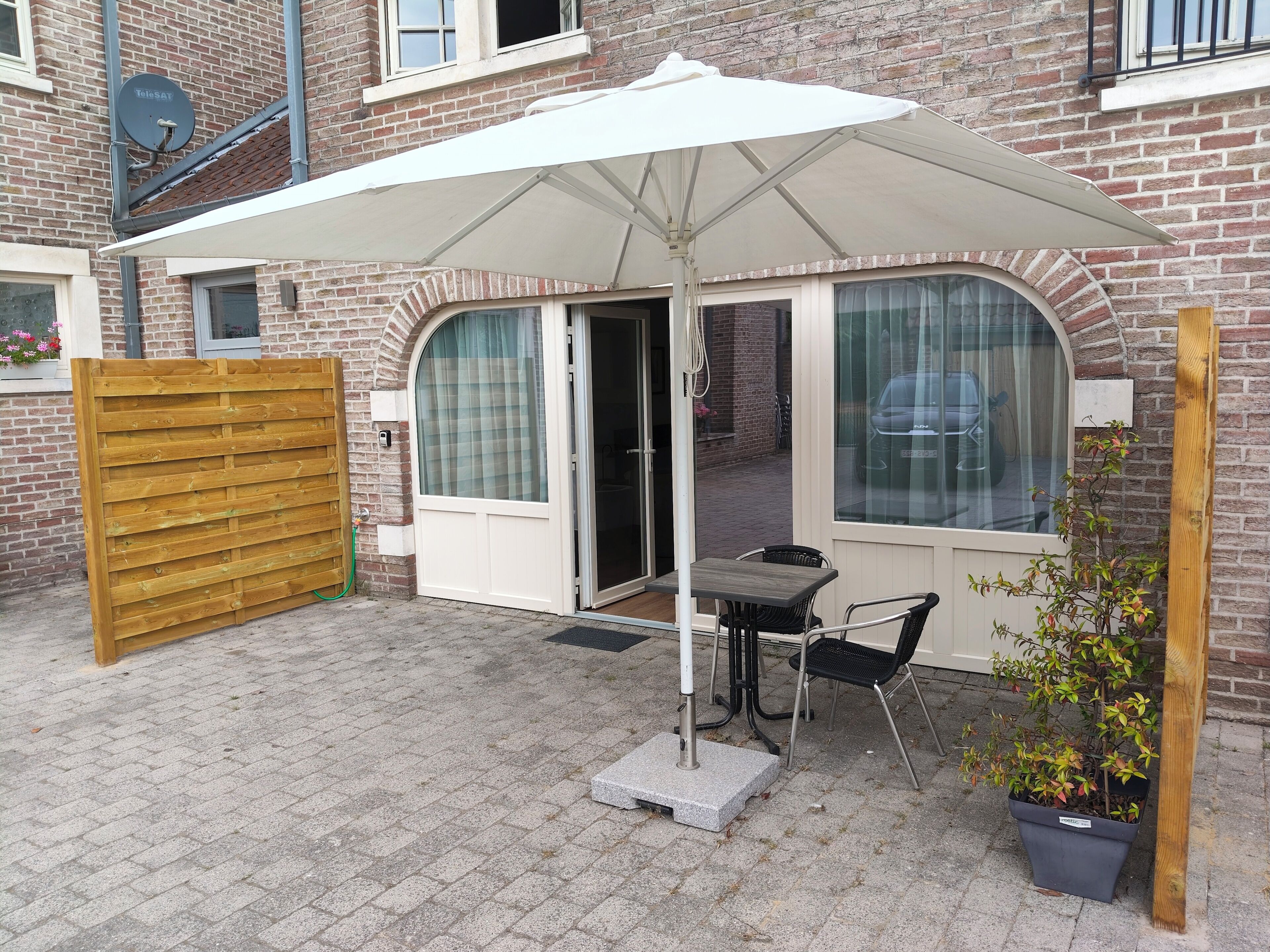 Une terrasse avec une table et des chaises, un parasol blanc et une plante en pot.