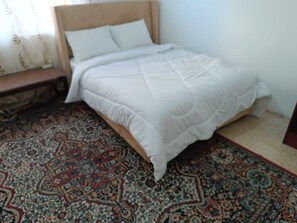 A bed with a white duvet, a patterned rug, and a wooden headboard. - Cozy 1-bedroom apartment in adorable Amman with AC (Amman)