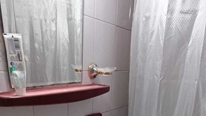 Casa de banho com lavatório de mármore branco, espelho, prateleira vermelha e cortina de chuveiro.