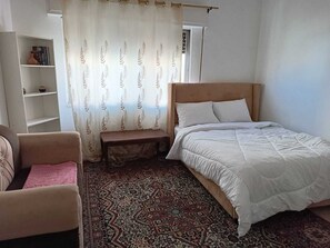 A bedroom with a bed, a bench, a chair, a shelf, and a patterned rug. - Cozy 1-bedroom apartment in adorable Amman with AC (Amman)