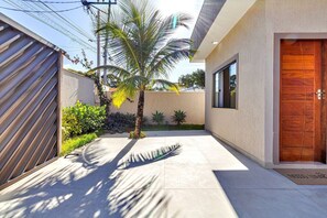 A modern building with a wooden door, a concrete pathway, and a palm tree. - House in Guriri, Cabo Frio – Space & Convenience (Cabo Frio)