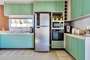A modern kitchen with teal cabinets, stainless steel appliances, and a built-in oven. - House in Guriri, Cabo Frio – Space & Convenience (Cabo Frio)