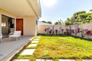 A modern outdoor patio with a white chair, a concrete pathway, and a wall with flowering plants. - House in Guriri, Cabo Frio – Space & Convenience (Cabo Frio)