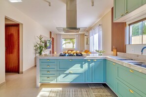 A modern kitchen with a central island, a built-in stove, and a window with curtains. - House in Guriri, Cabo Frio – Space & Convenience (Cabo Frio)