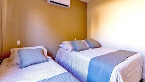 Une chambre avec deux lits, chacun équipé d’un oreiller et d’une couverture. Un climatiseur mural est fixé au-dessus des lits.