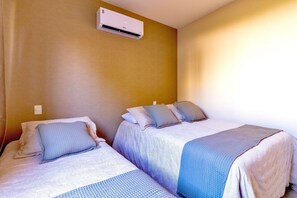 A room with two beds, each with a pillow and a blanket. There is a wall-mounted air conditioning unit above the beds. - House in Guriri, Cabo Frio – Space & Convenience (Cabo Frio)