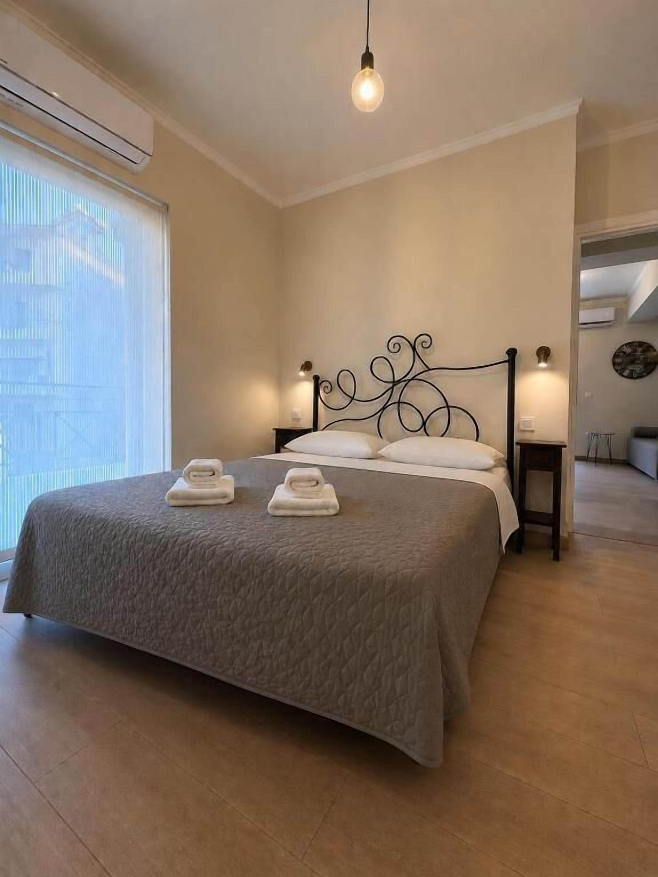 Quarto de hotel com cama, luminárias de cabeceira, janela com persianas e vista para o exterior.