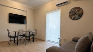 Una sala moderna con un sofá, una mesa de comedor, sillas y un televisor de pantalla plana montado en la pared.