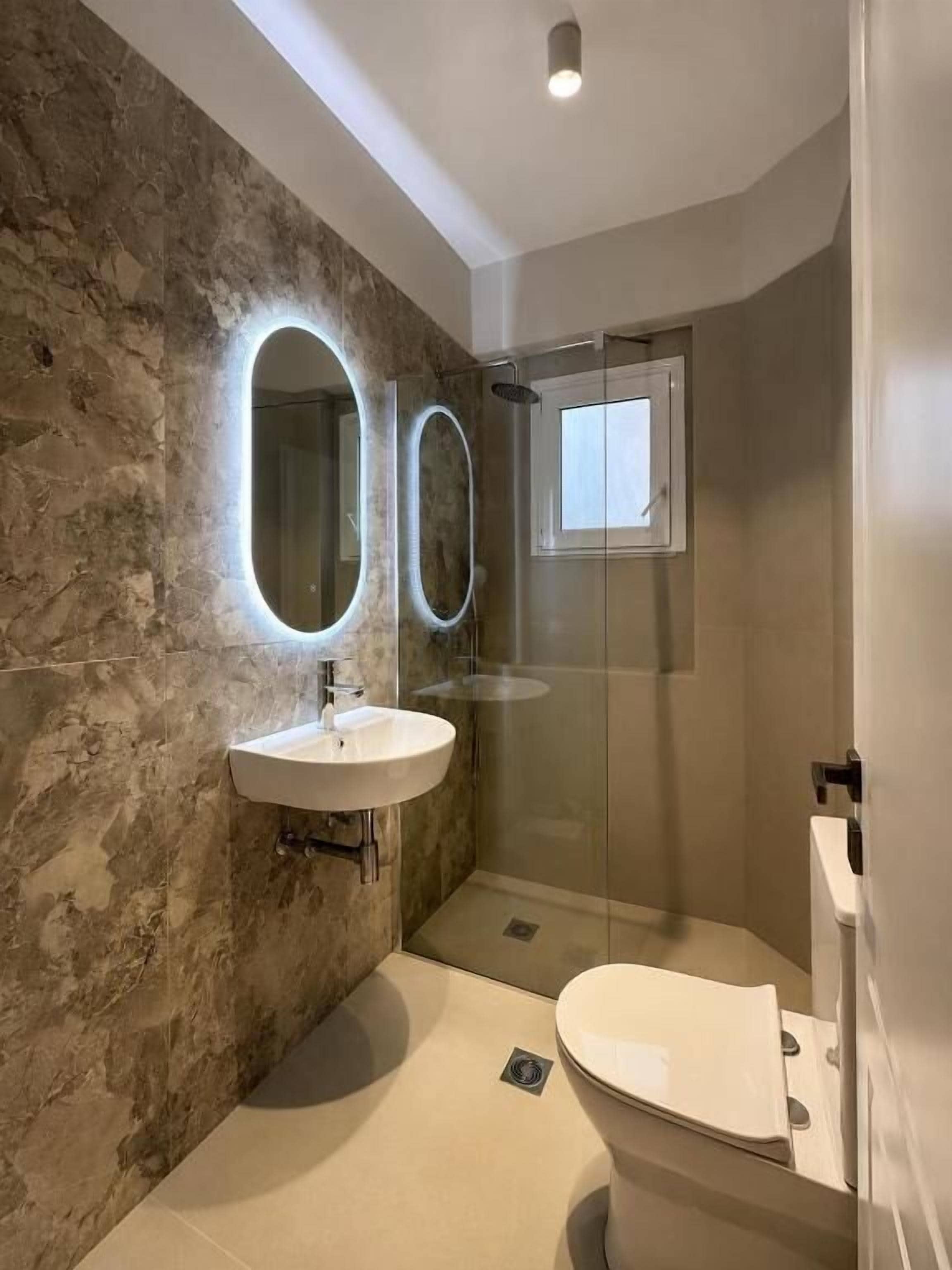Un baño con pared de piedra, un lavabo blanco, un espejo, cabina de ducha de vidrio y un inodoro.