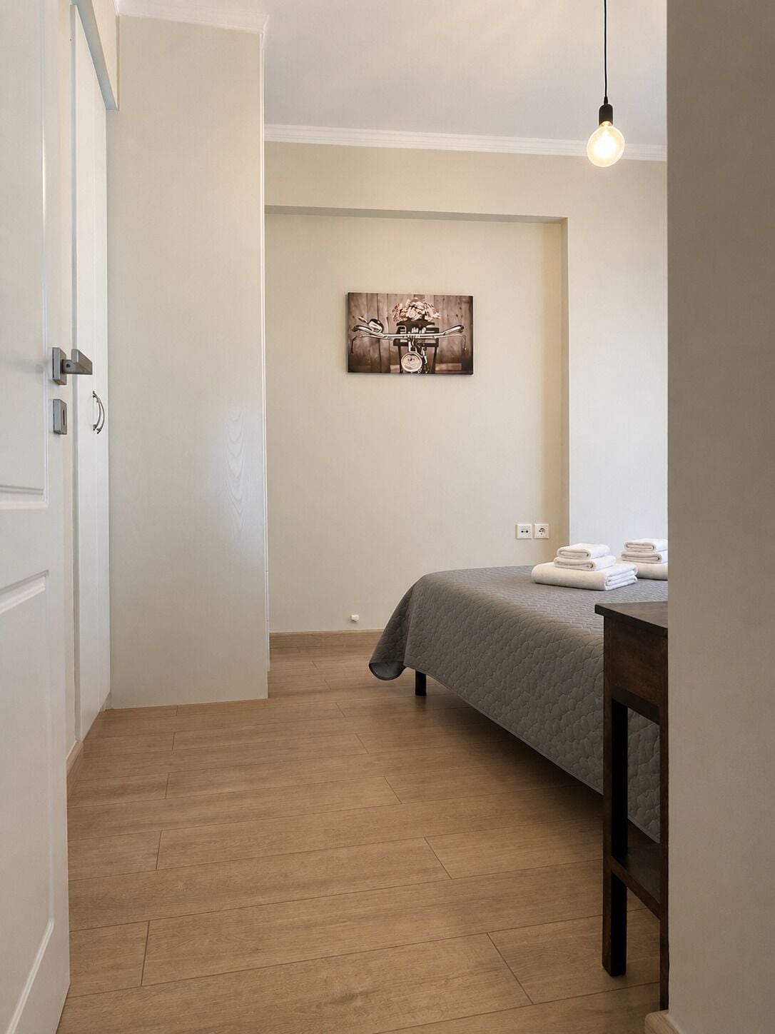 Une chambre à coucher comprenant un lit, une table de chevet avec des serviettes, une œuvre d’art accrochée au mur et un luminaire suspendu.