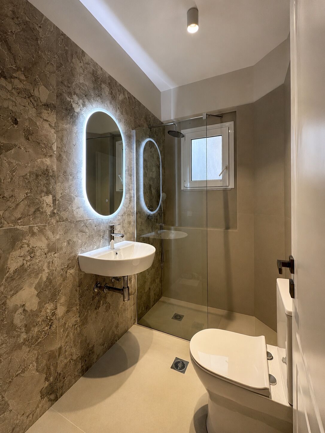 Un baño moderno con pared de mármol, un lavabo, un inodoro y una cabina de ducha.
