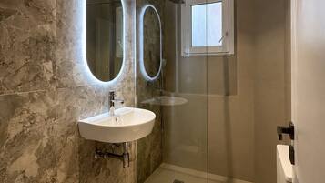 Un baño moderno con pared de mármol, un lavabo, un inodoro y una cabina de ducha.