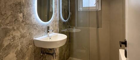 Un baño moderno con pared de mármol, un lavabo, un inodoro y una cabina de ducha.