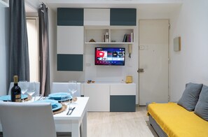 A modern living room with a flat-screen TV mounted on the wall, a dining area with a table set for two, and a bed with a yellow blanket. - SANTA CECILIA HOUSE, CENTRO, PALERMO-350, MT, STATION (Palermo)