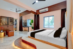 A modern bedroom with a large bed, a ceiling fan, an air conditioning unit, a desk, and a window with a view.