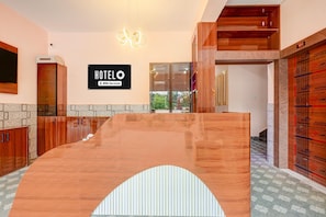 Zona de recepción de hotel con mostrador de madera, un cartel que indica que ofrece servicios OYO y vistas al exterior a través de un vidrio.