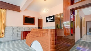 Un espace d’accueil d’hôtel avec un comptoir de réception en bois, une horloge numérique et un panneau indiquant que l’hôtel est affilié à la chaîne OYO.