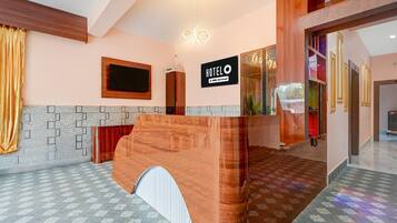 Un espace d’accueil d’hôtel avec un comptoir de réception en bois, une horloge numérique et un panneau indiquant que l’hôtel est affilié à la chaîne OYO.