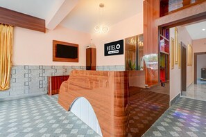 A hotel reception area with a wooden reception desk, a digital clock, and a sign indicating the hotel is serviced by OYO.