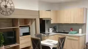 A modern kitchen with wooden cabinets, a dining table with chairs, a television, and a clock on the wall.