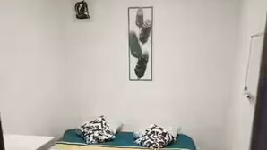 A narrow room with a bed, a framed picture on the wall, and a door on the right.