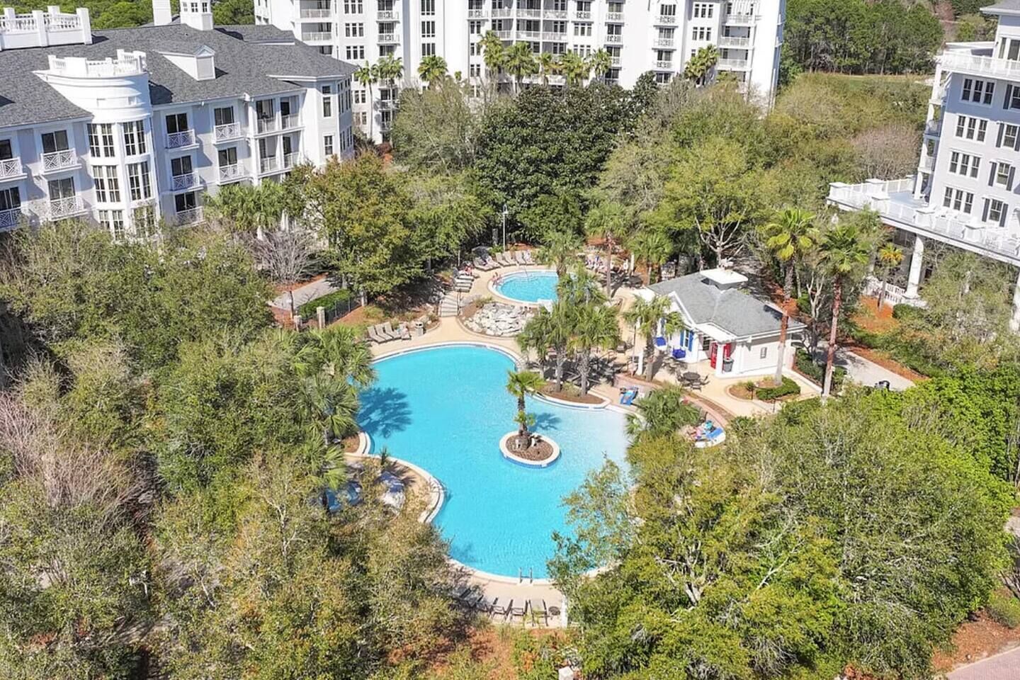 Un resort con piscina central rodeada de palmeras y un edificio de varios pisos con balcones.