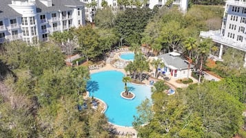 Un resort con piscina central rodeada de palmeras y un edificio de varios pisos con balcones.