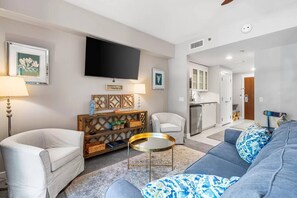 A living room with a sofa, armchairs, a coffee table, and a TV. There is a kitchen area visible in the background. - Luxury Baytowne Wharf- Bahia Breeze -Pool View (Miramar Beach)