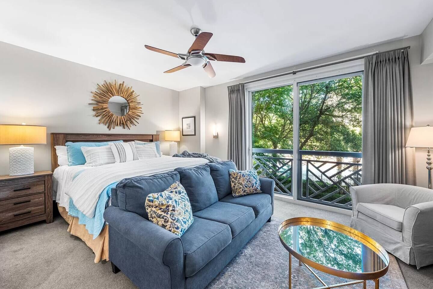 A modern bedroom with a bed, a blue sofa, a round coffee table, and a balcony with curtains.