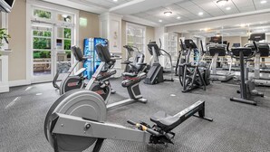 Ein Fitnessstudio mit unterschiedlichen Trainingsgeräten, darunter Laufbänder und Ergometer, und einem großen Fenster, das für natürliches Licht sorgt.