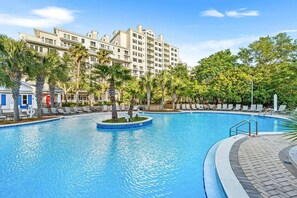 A swimming pool with a circular section, surrounded by lounge chairs and palm trees, with a multi-story building in the background. - Luxury Baytowne Wharf- Bahia Breeze -Pool View (Miramar Beach)
