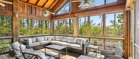 A covered outdoor seating area with a wooden ceiling, large windows, and a ceiling fan.