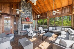 An outdoor covered patio with stone walls, a fireplace, wicker furniture, and large windows offering a view of the outdoors. - Luxury Baytowne Wharf- Bahia Breeze -Pool View (Miramar Beach)