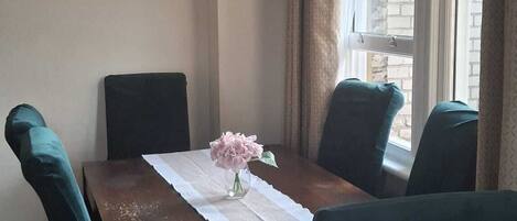 A dining area with a table set for four, chairs, a chandelier, a painting, and a window with curtains.