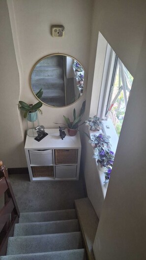 Un escalier menant à un palier agrémenté d’une console blanche, d’un miroir rond et de plantes en pot.