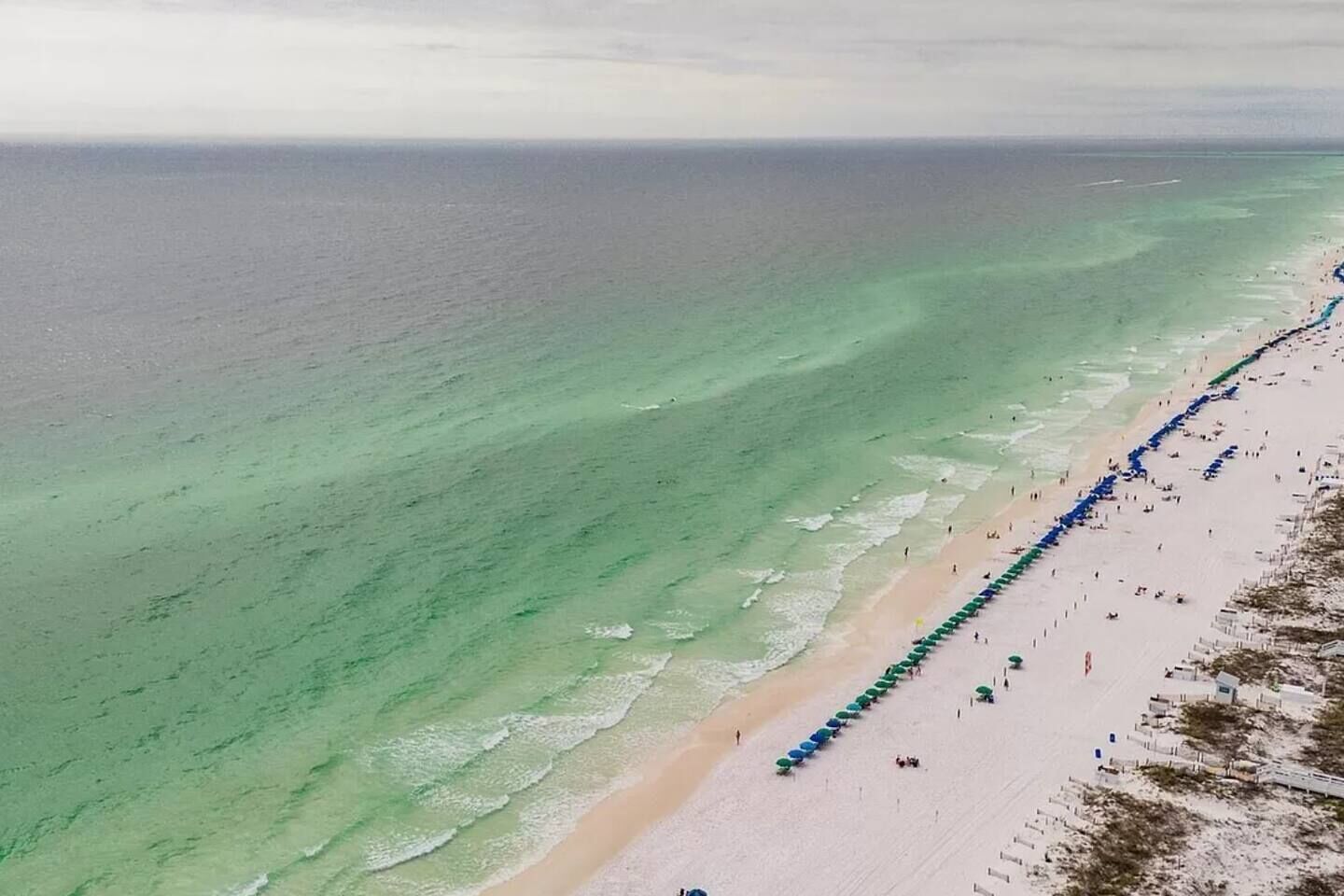 Ein Strand mit einer langen Reihe von Sonnenschirmen und Menschen.